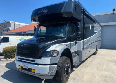 A large, black and silver DYNAMAX DX3 RV parked outside a detailing shop on a sunny day.