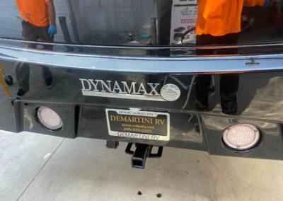 Close-up of a DYNAMAX RV rear with Demartini RV dealership plate and reflective black surface.