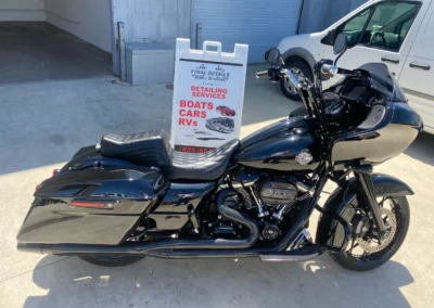 Black Harley-Davidson touring motorcycle parked next to mobile detailing service sign at business lot.