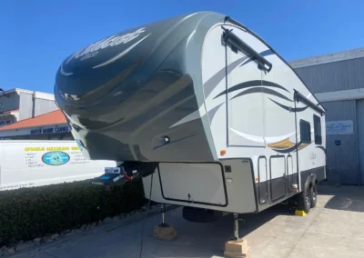 Large fifth-wheel RV trailer with gray/white exterior parked at dealership with stabilizing jacks down.RetryClaude can make mistakes. Please double-check responses.