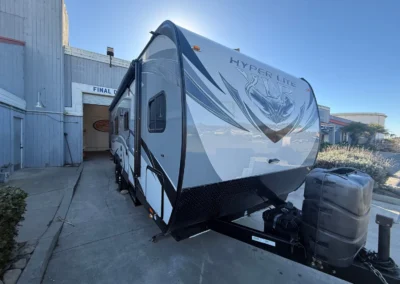 Modern white/gray travel trailer "Hyper Lite" parked outside RV dealership with propane tanks attached