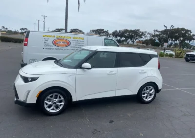 A clean white compact SUV parked beside a mobile detailing service van in a lot with cloudy skies.