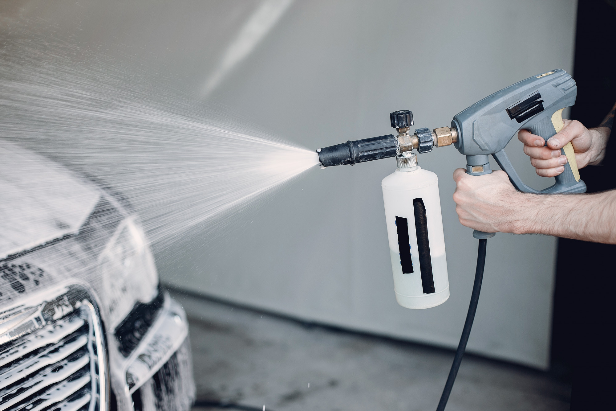 A person using a pressure washer with a foam cannon to clean a car