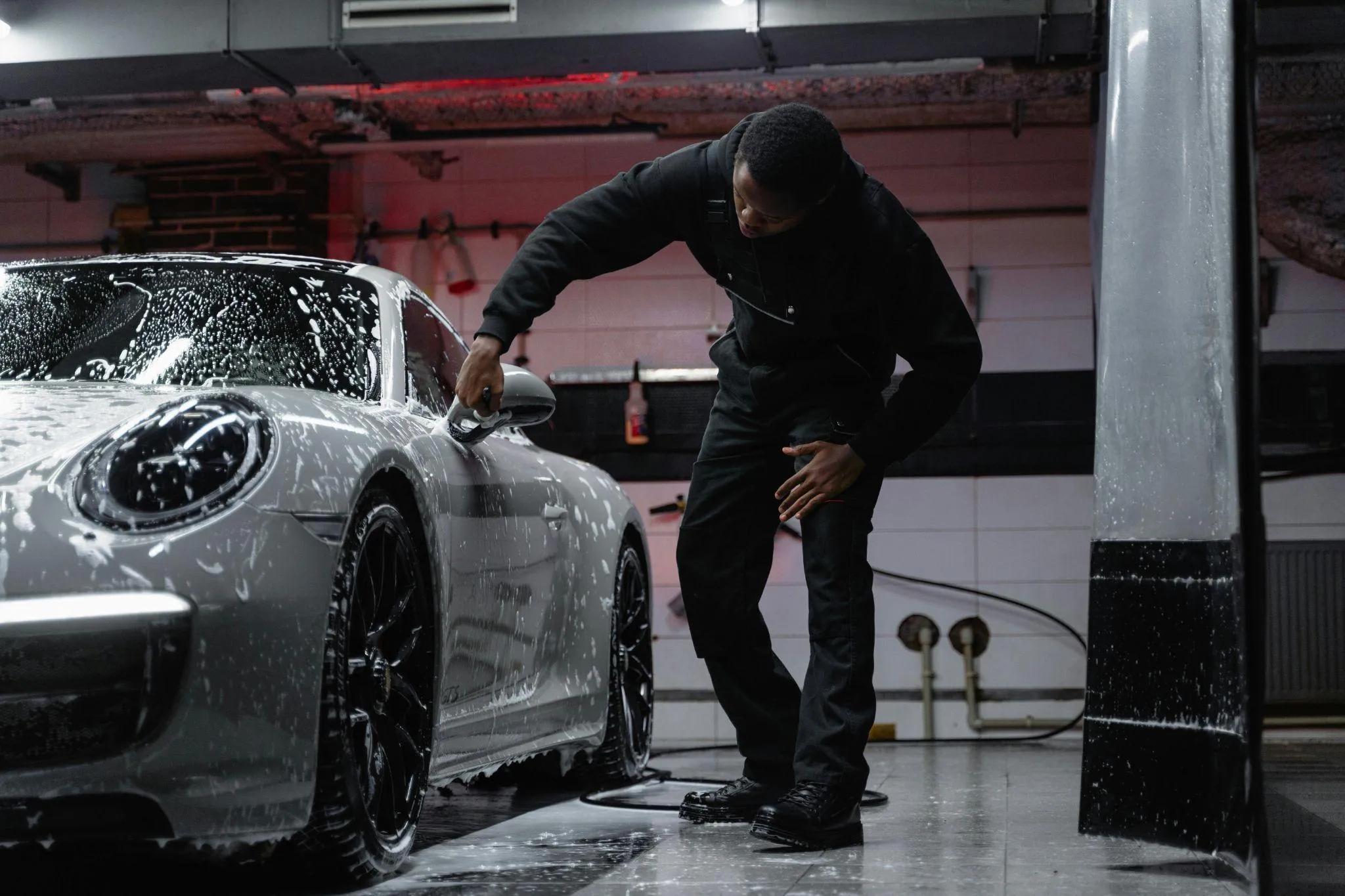 Detailer washing a white sports car in the garage.